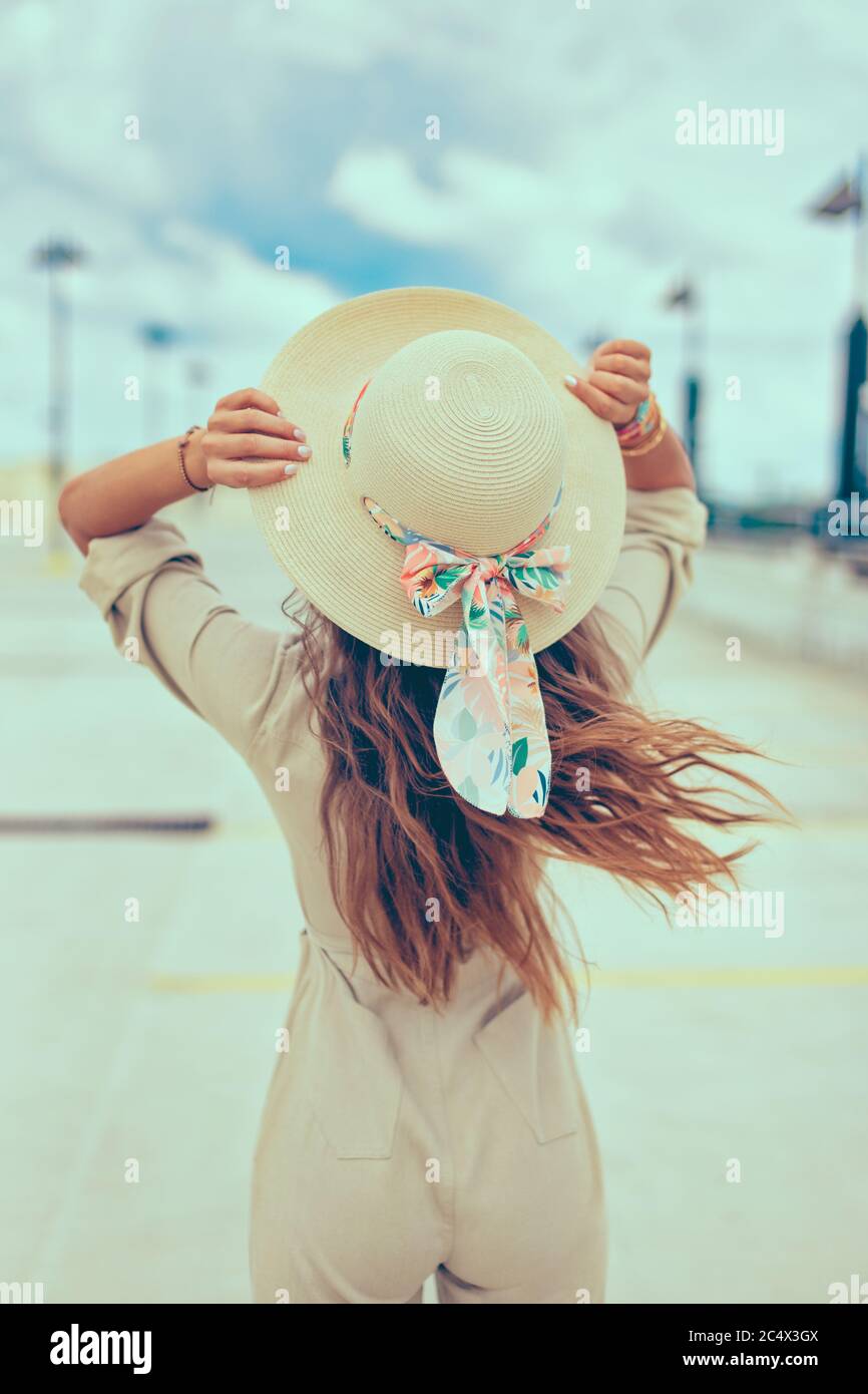 Mujer sin preocupaciones sosteniendo sombrero vista trasera exterior, feminidad y verano Foto de stock