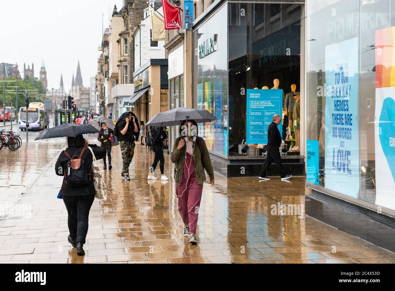 Edimburgo, Escocia, Reino Unido. 29 de junio de 2020. Muchas tiendas que tienen acceso a la calle tienen permitido abrir para negocios en Escocia hoy. A pesar de las temperaturas frías, los vientos fuertes y a menudo las lluvias fuertes, algunas tiendas tenían colas afuera por la mañana. Las tiendas de turismo en la Royal Mile permanecieron cerradas, sin embargo, debido a la falta de turistas, y las calles en el casco antiguo permanecieron vacías. En la foto, los compradores se enfren a la lluvia en Princes Street. Iain Masterton/Alamy Live News Foto de stock