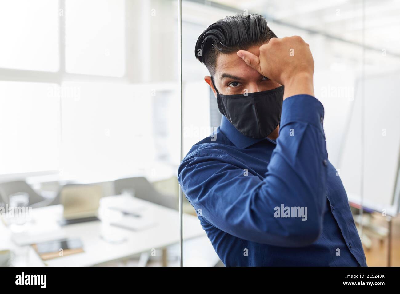 Estresado hombre de negocios en la oficina usando una máscara debido a Covid-19 y la pandemia de coronavirus Foto de stock