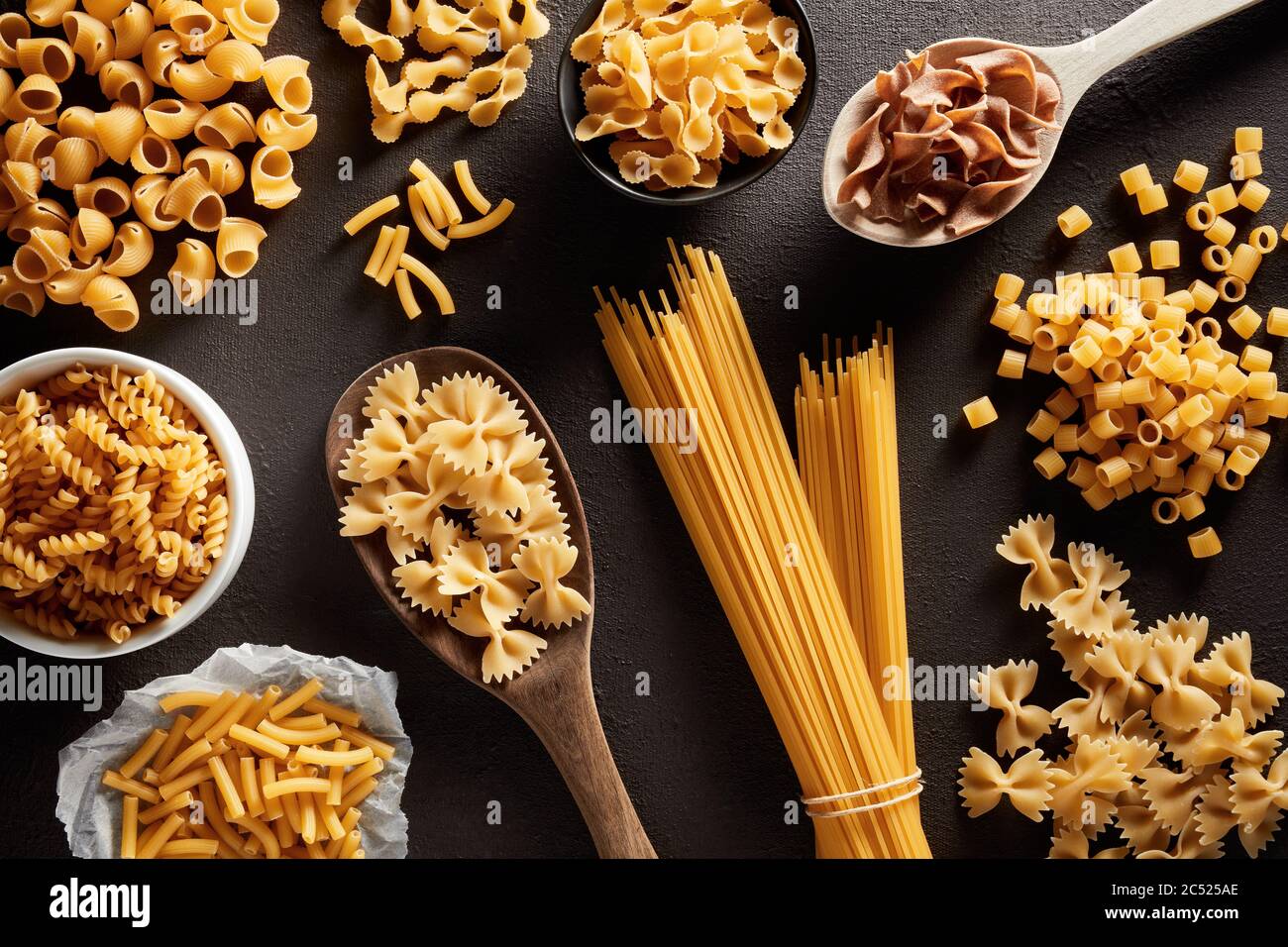 Montón de varias pastas crudas en diferentes tipos y formas sobre fondo marrón oscuro. Vista de gastos generales. Foto de stock