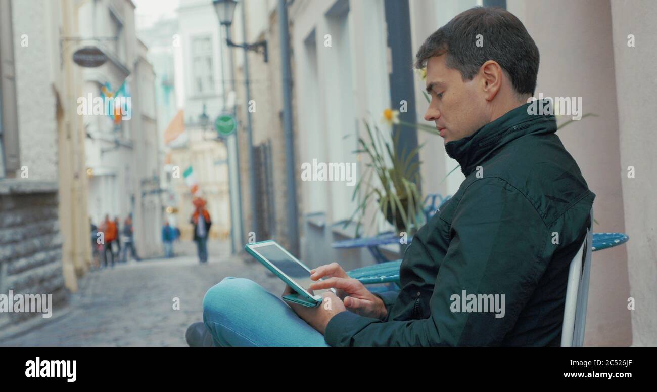 Perfil de vista de hombre adulto trabajando en su tableta al aire libre en la pequeña calle de la ciudad. Tallin, Estonia Foto de stock