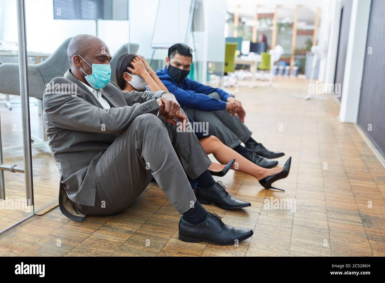 La gente triste de negocios con máscara se sienta en el piso de la oficina después de un trabajo de corta duración o de un trabajo de corta duración Foto de stock