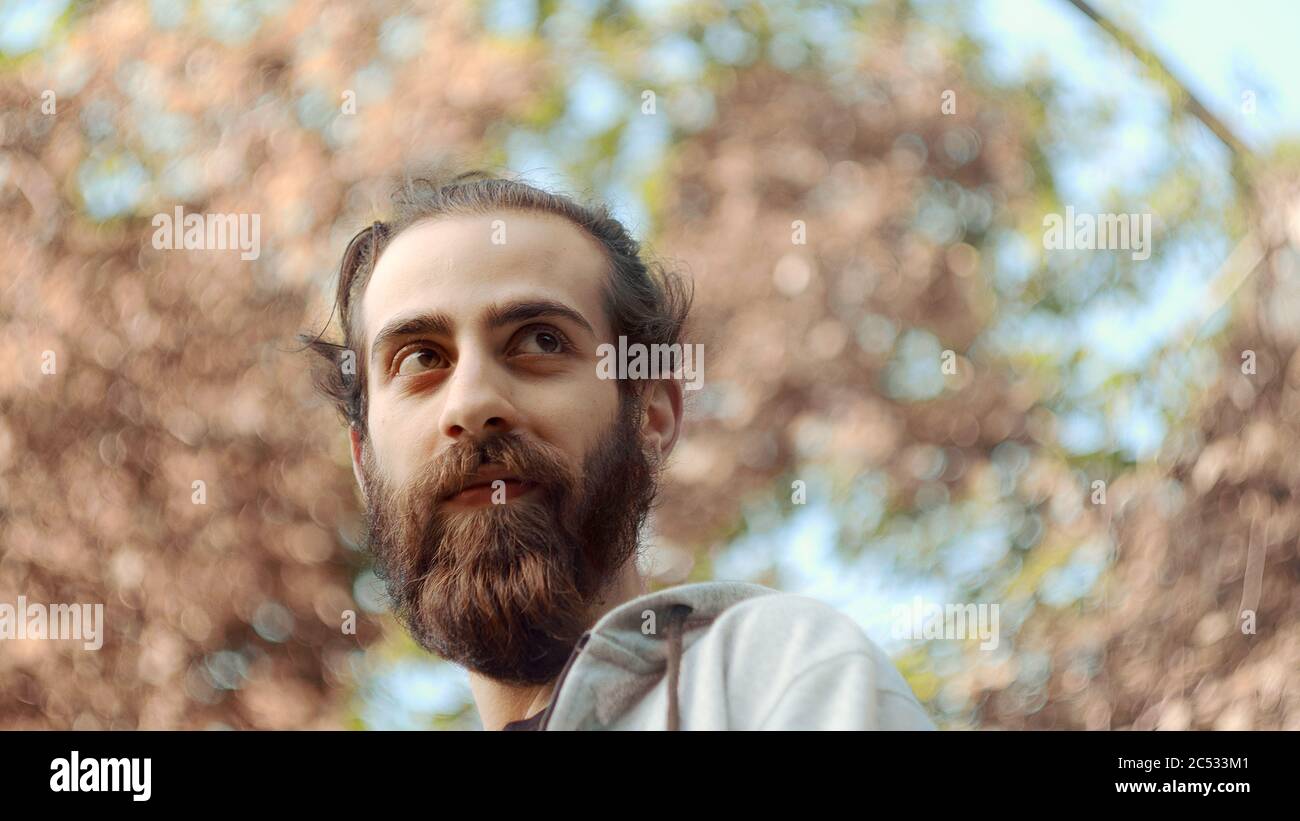 Joven de pelo largo largo de barba largo de cintura baja con barba tomando un profundo aliento mirando detrás de él Foto de stock