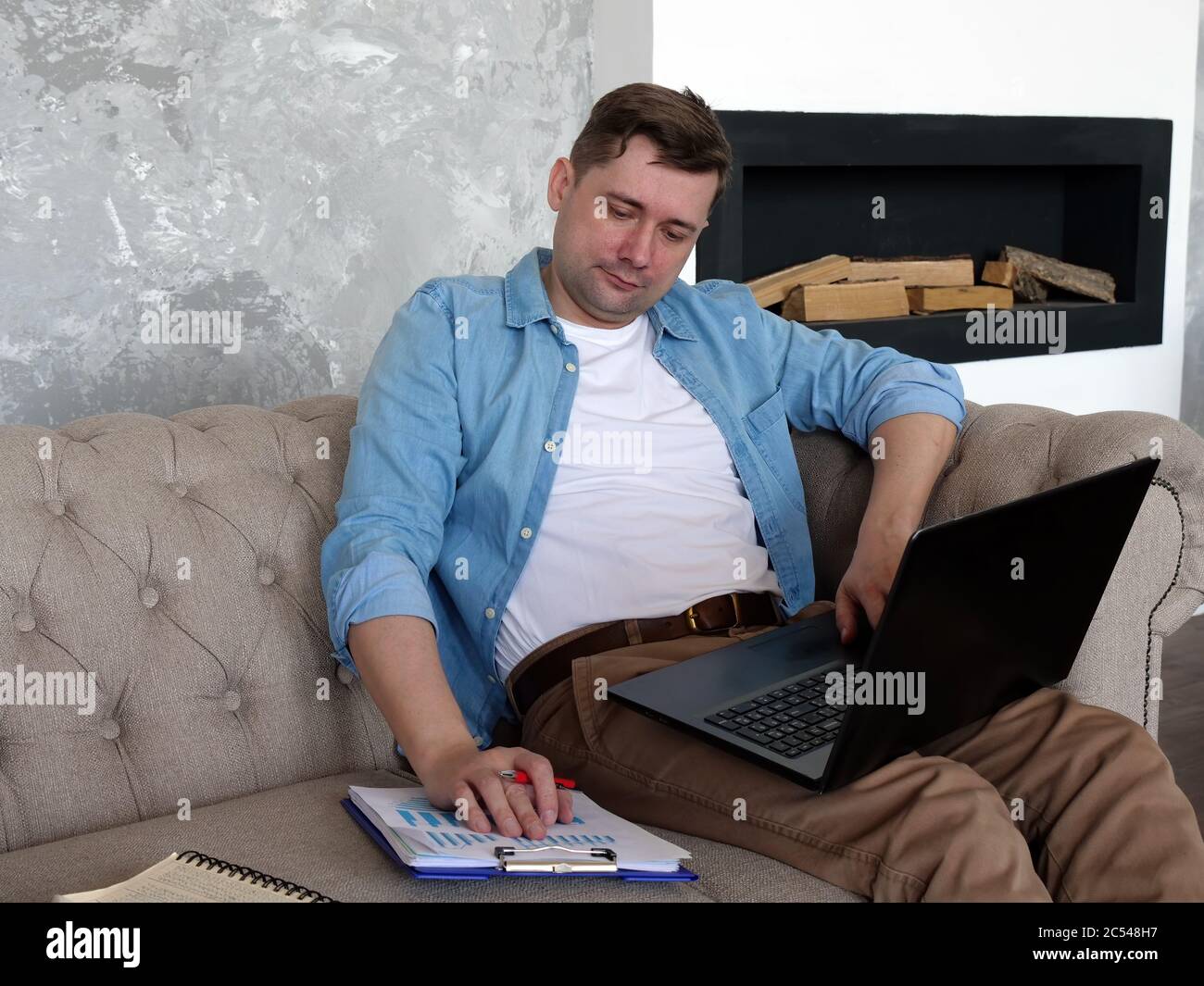 Concepto de cuarentena. El tipo en casa en el sofá revisa el informe financiero. Foto de stock