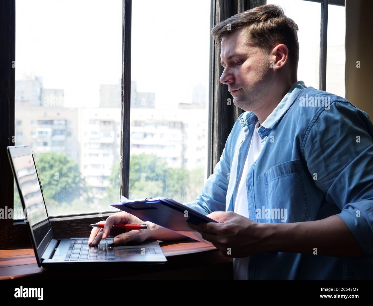 Cuarentena y teletrabajo. El joven freelancer trabaja en la ventana. Foto de stock