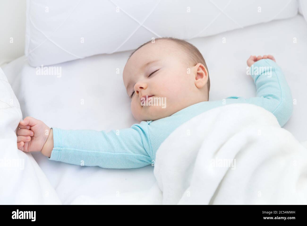 Bebé durmiendo con un chupete aparte. Pijama azul claro y sábanas blancas. Foto de stock
