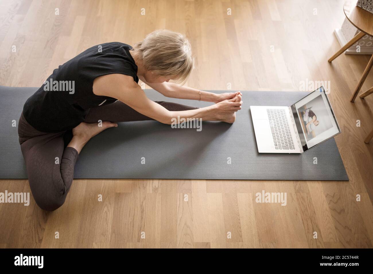 Mujer 40+ practica yoga en casa con cuaderno. Clase de yoga en línea. Foto de stock
