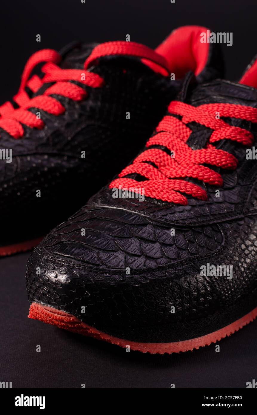 Modernas sneakers de piel de serpiente. Sneakers negras con cordones rojos  brillantes sobre fondo negro y rojo y sombras largas Fotografía de stock -  Alamy