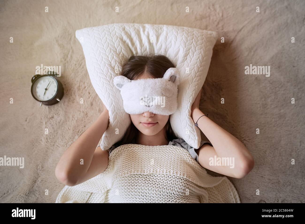 Una adolescente soñolienta que apaga la alarma por la mañana mientras está acostada en la cama Foto de stock
