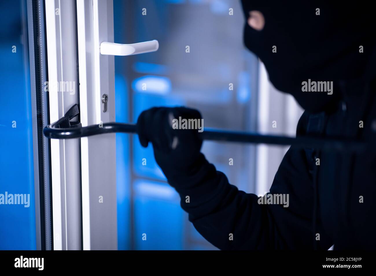 Ladrón en negro balaclava puerta de grietas con la crowbar Foto de stock