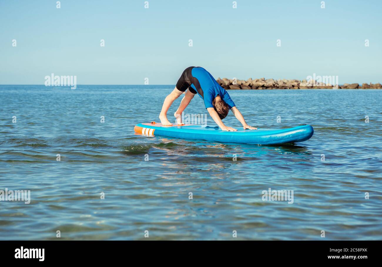 Adolescente en traje de neopreno haciendo yoga en el tablero de SUP en el  mar Báltico. Posición de perro Fotografía de stock - Alamy
