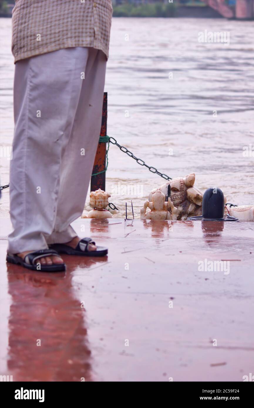Un hombre pies con pijama blanco y calzado indio de pie junto al río Ganga y la escultura de Dios en Haridwar, India Foto de stock