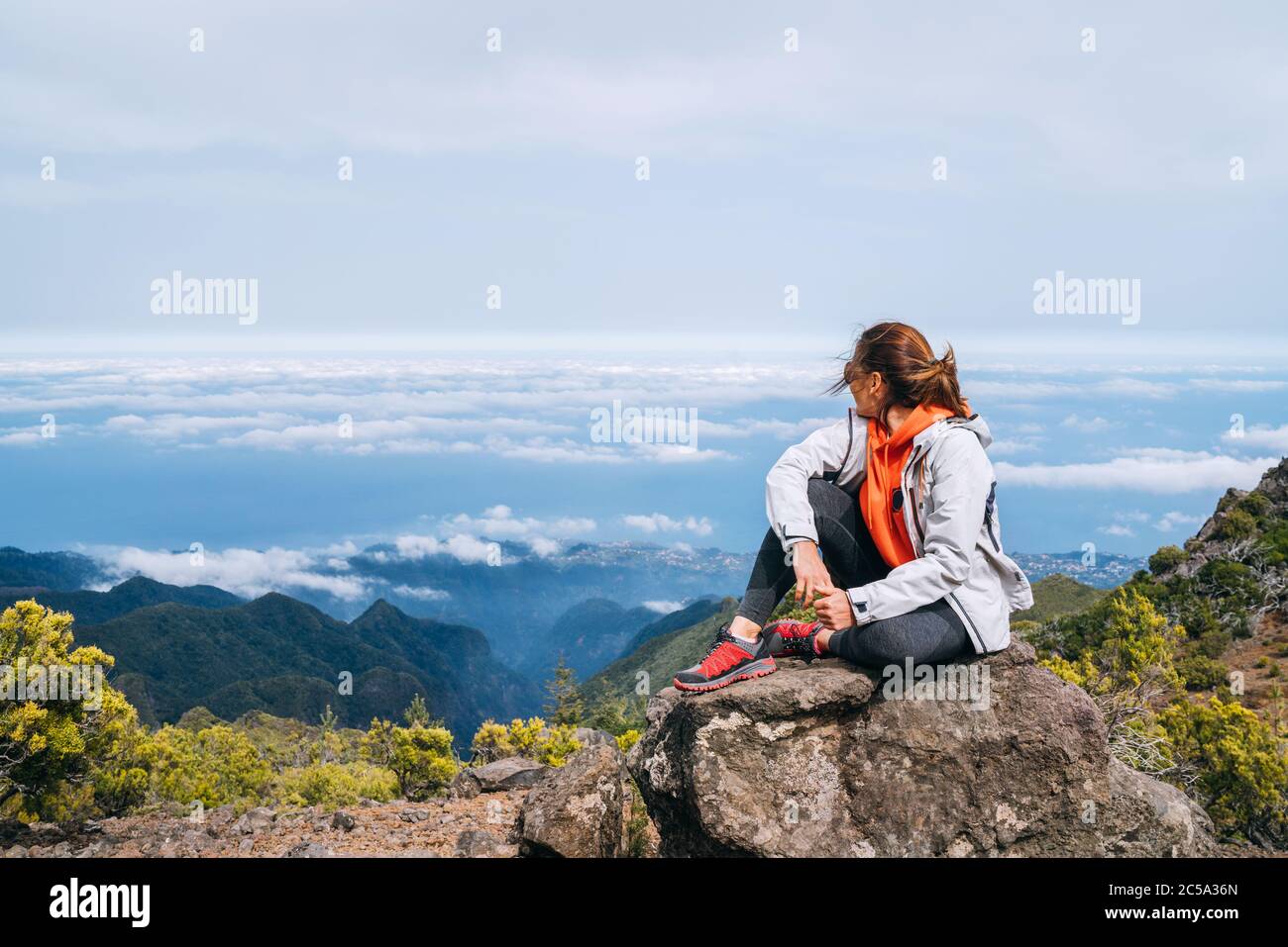 Joven adulto mujer caucásica vestida ropa deportiva descansando en la roca  y disfrutando de las nubes vista desde el Pico Ruivo monte 1861m - el pico  más alto en TH Fotografía de