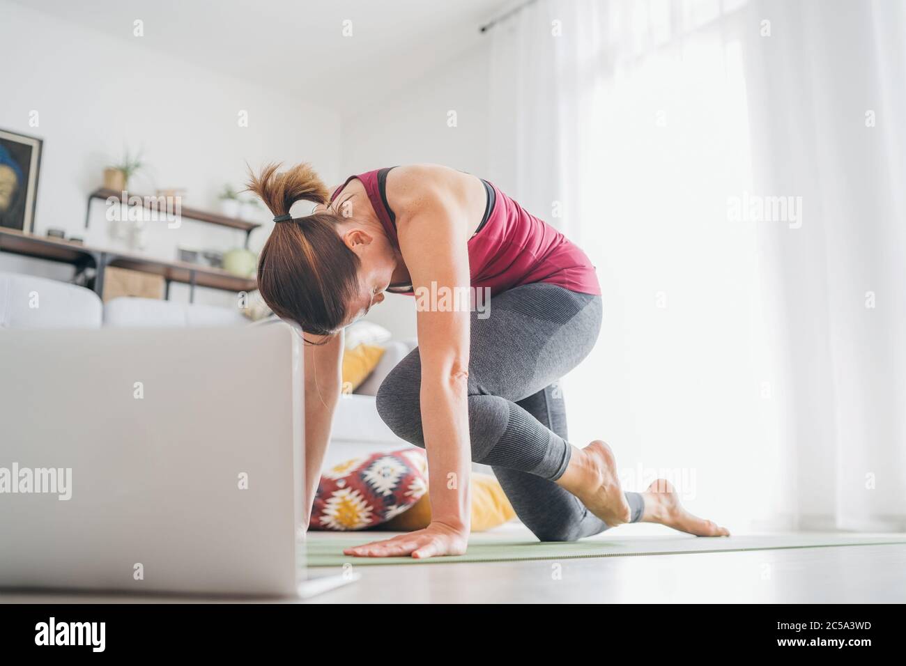 Ajuste a la mujer caustiana sana deportiva en una estera de yoga, haciendo ejercicios de respiración, viendo clases de yoga en línea en un ordenador portátil. Personas sanas y. Foto de stock