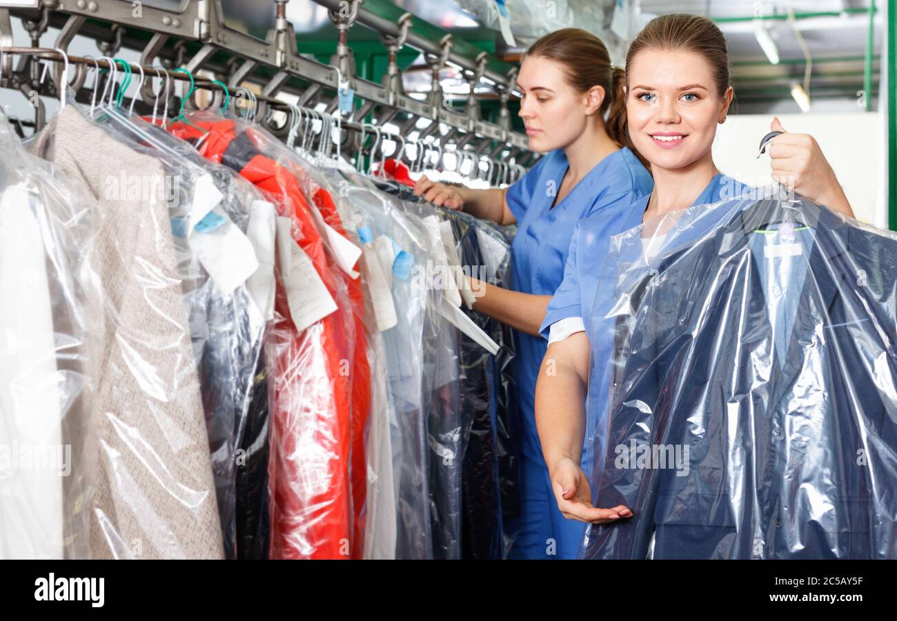 Trabajador alegre de la mujer diligente segura de la tintorería mostrando  ropa limpia en bolsa de plástico de la ropa Fotografía de stock - Alamy