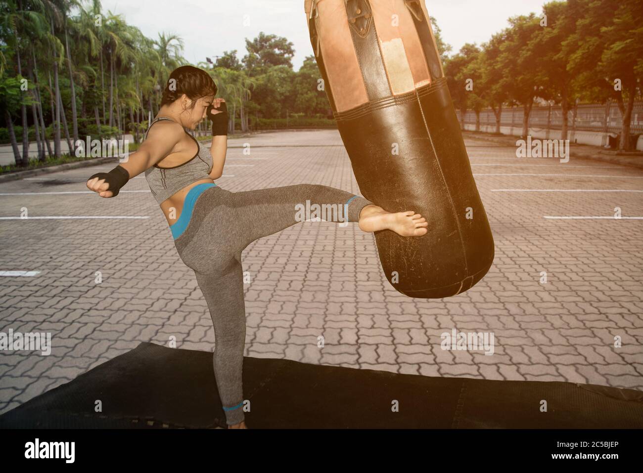 Hermosa niña blanca asiática joven con pelo largo de 20-30 años de edad. Práctica Muay Thai boxing pateando en el Boxing Sandbag en el parque. Foto de stock