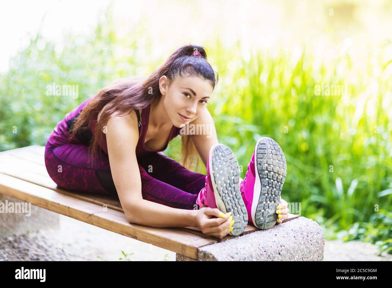 Una hermosa atleta realiza un ejercicio en un banco en el parque en una cálida mañana de verano. Concepto de estilos de vida saludables Foto de stock