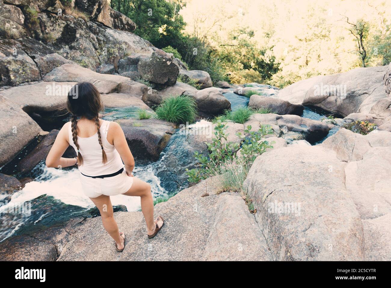 Rubia chica con brádas mirando la cascada correr. Foto de stock