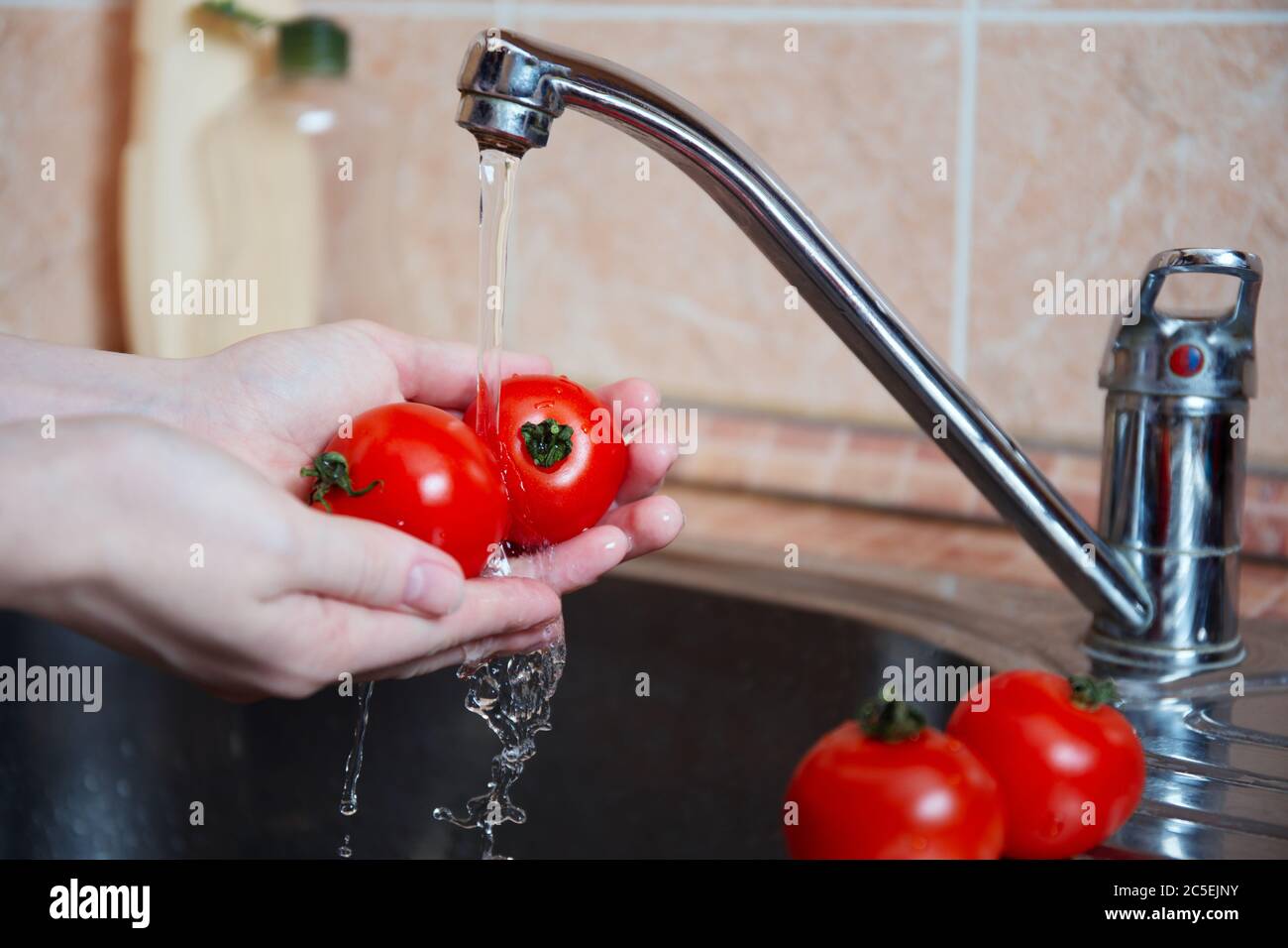 Verduras frescas o tomates jugosos bajo el agua corriente. Las manos femeninas lavan verduras frescas. Concepto de higiene y cuidado personal. Foto de stock