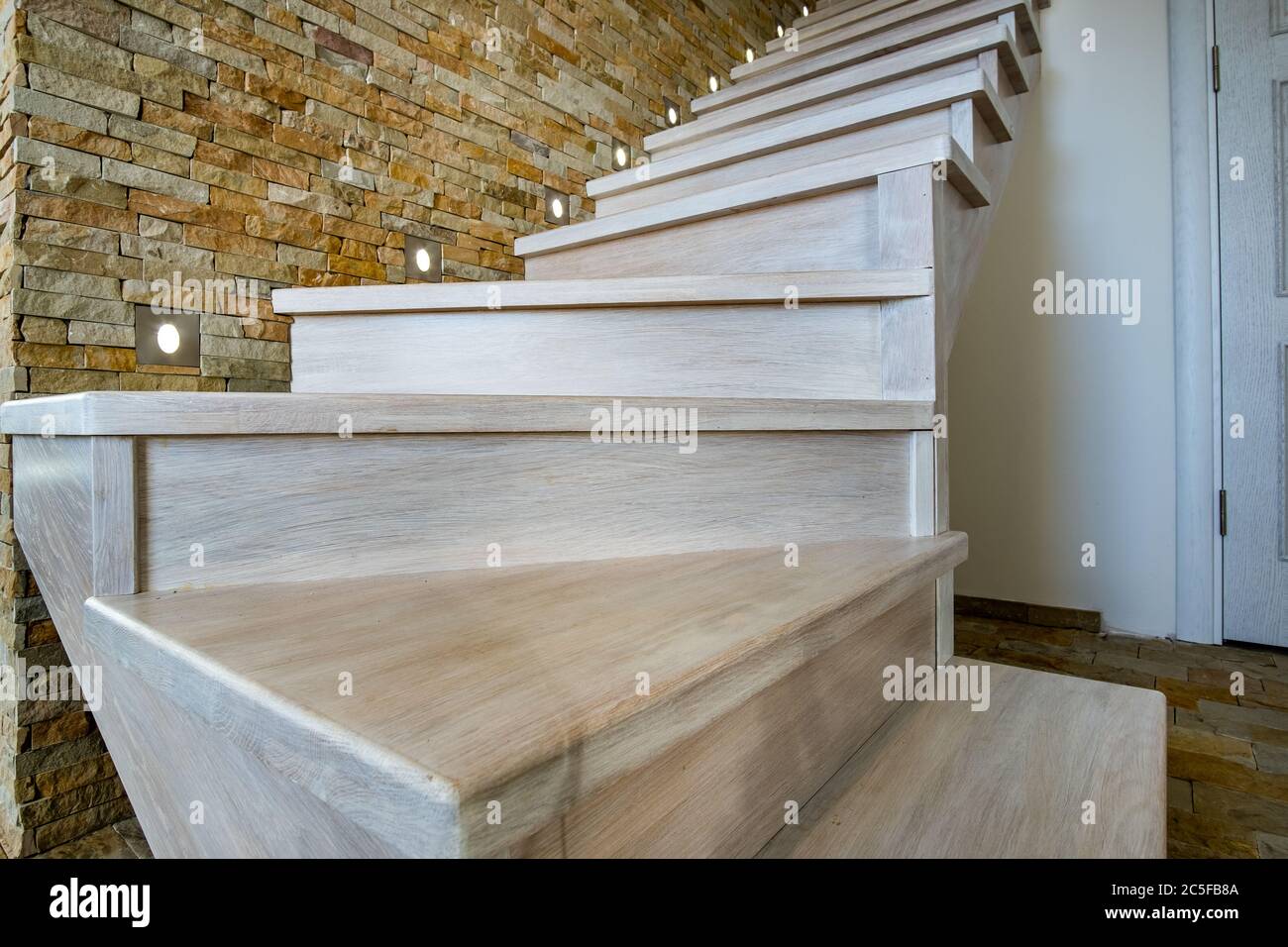 Elegante escalera contemporánea de madera en el interior de la casa loft. Pasillo moderno con paredes decorativas de ladrillo de piedra caliza y escaleras de roble blanco. Foto de stock