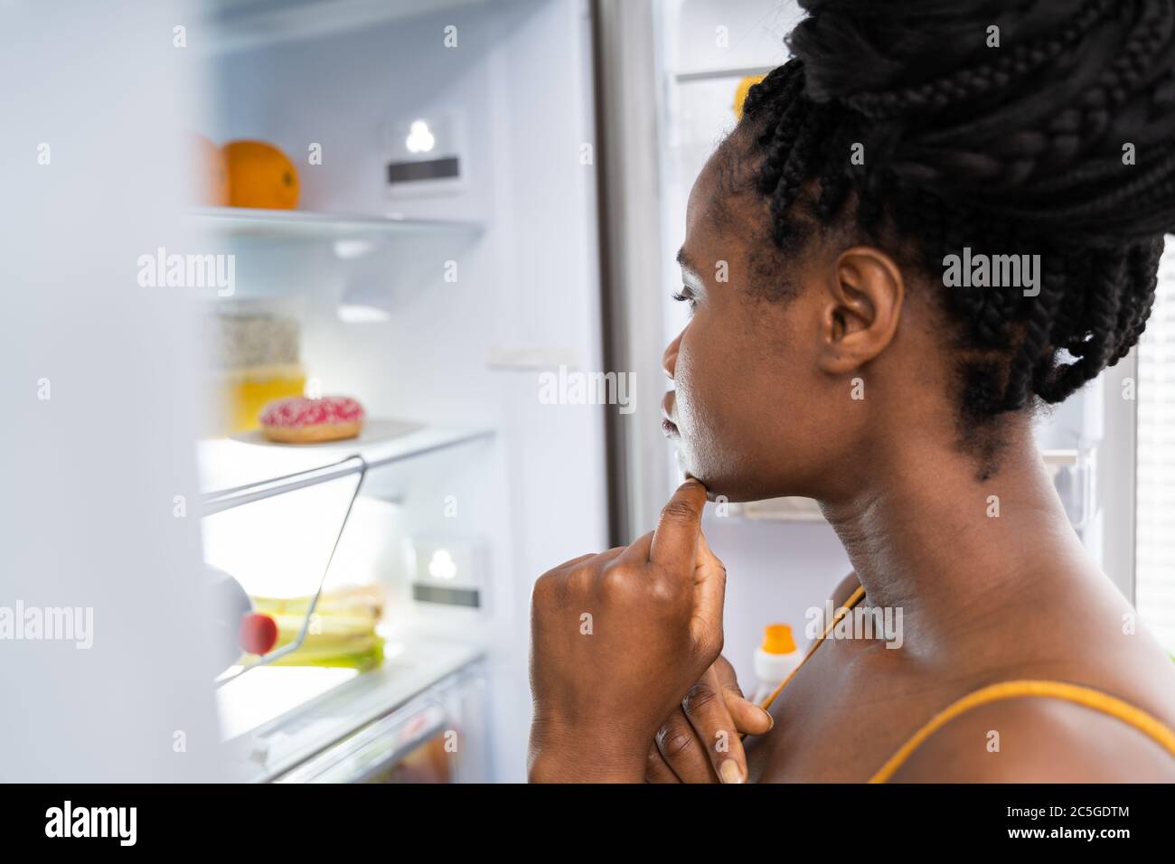 Mujer africana piensa en la comida cerca del refrigerador en la cocina Foto de stock