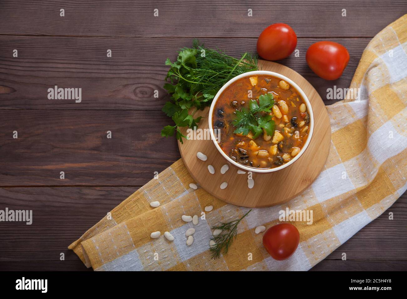 Sopa de frijoles con verduras y queso en una taza de cerámica sobre una servilleta de lino amarillo, sobre una mesa de madera. Comida vegetariana. Plano. Copiar espas Foto de stock