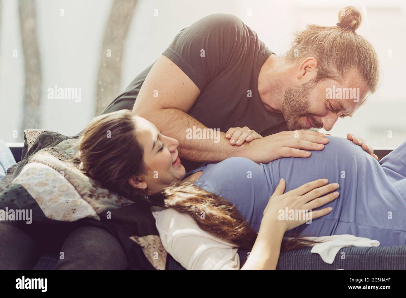 Buen marido y mujer embarazada con amor romántico momento juntos besando el vientre del bebé en casa suave luz del sol de la mañana. Foto de stock
