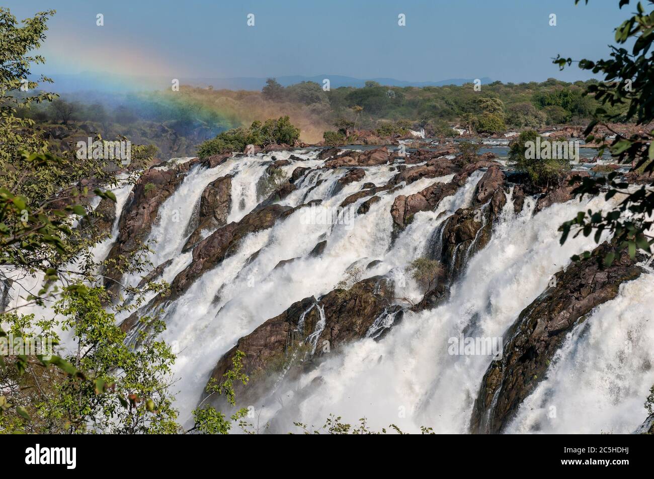 Parte de la cascada de Ruacana en el río Kunene. Un arco iris y libélulas son visibles Foto de stock