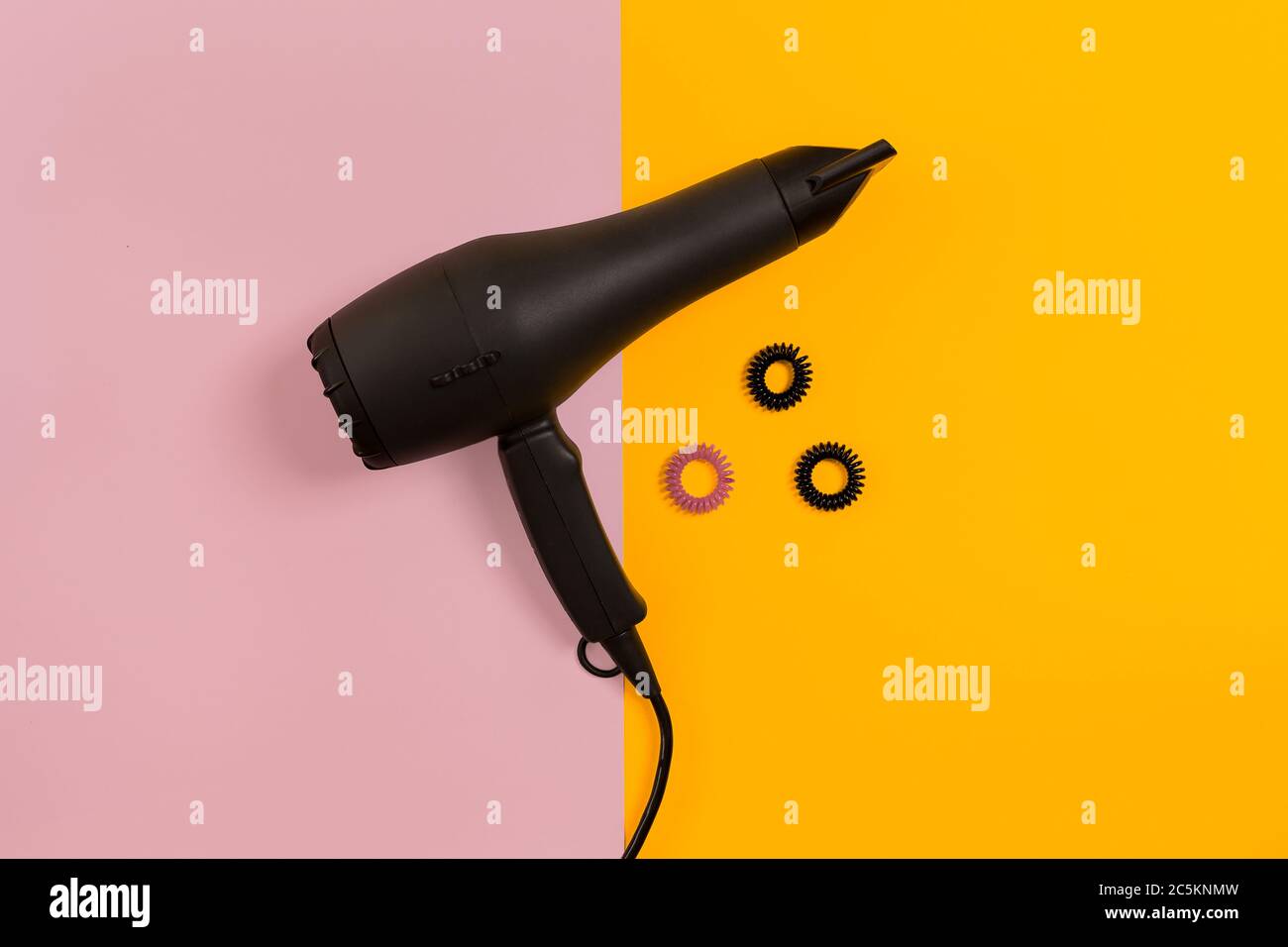 Secador de pelo negro sobre fondo de papel rosa y amarillo. Vista superior  Fotografía de stock - Alamy