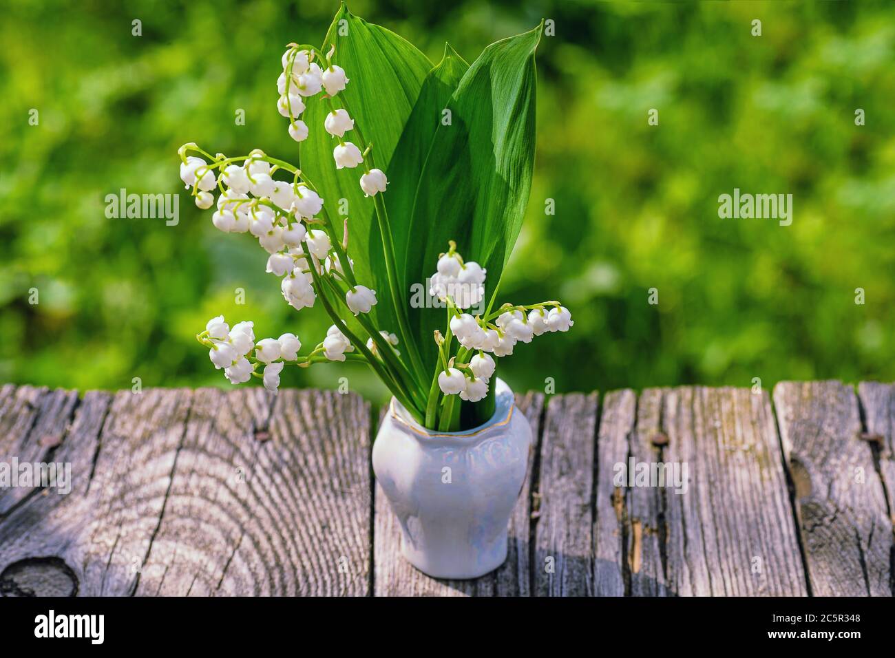 Ramo de flores de primavera de pie en un jarrón sobre una mesa de madera con copia espacio.Lily del valle. Flor Primavera Sol Blanco Verde Fondo horizontal Foto de stock