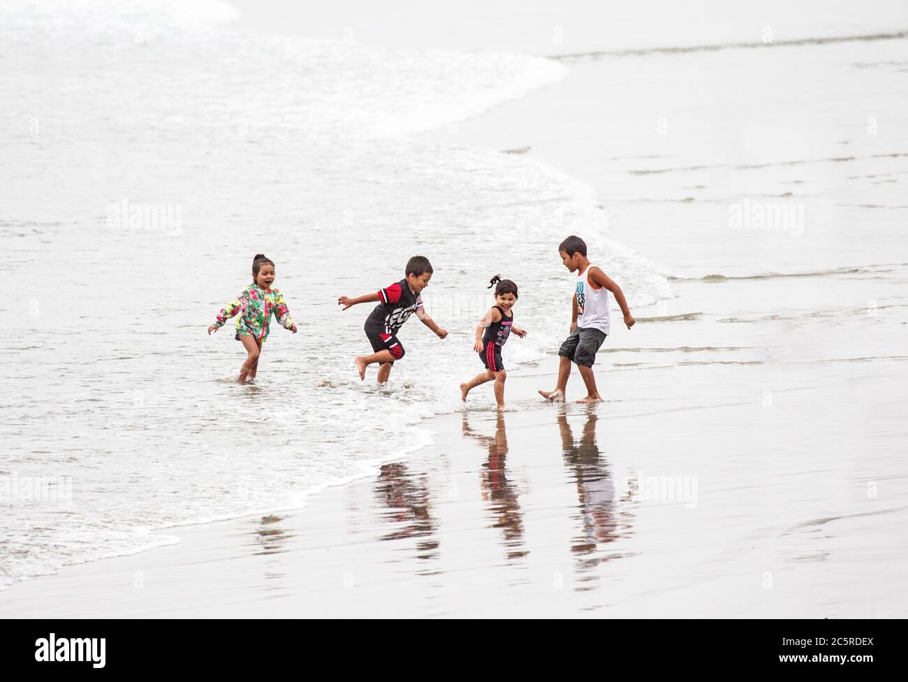 Cuatro niños pequeños corriendo de Incoming Surf Foto de stock