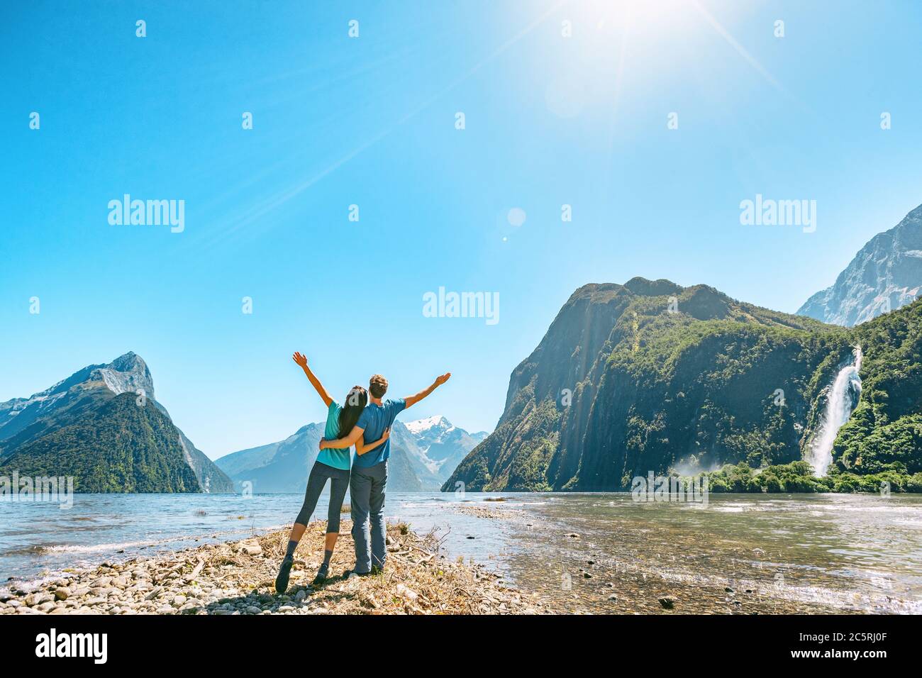 Una pareja al aire libre feliz con los brazos estirados en Milford Sound New Zelanda en la naturaleza disfrutando de un activo estilo de vida al aire libre senderismo en Milford Suena nuevo Foto de stock