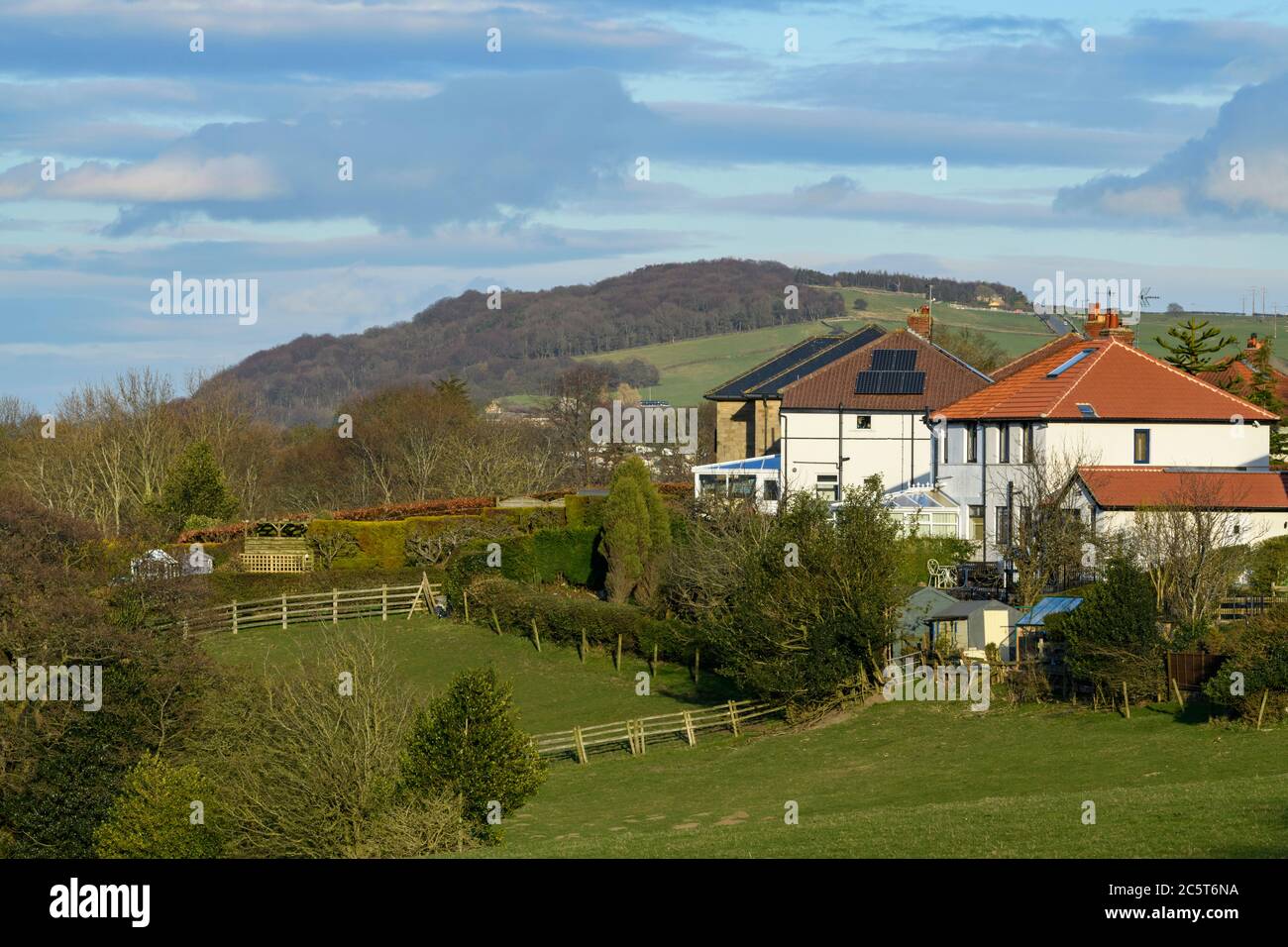 Casas adosadas en barrios verdes, campos de granja y Otley Chevin (bosque de ladera) - Menston Village, West Yorkshire, Inglaterra, Reino Unido. Foto de stock