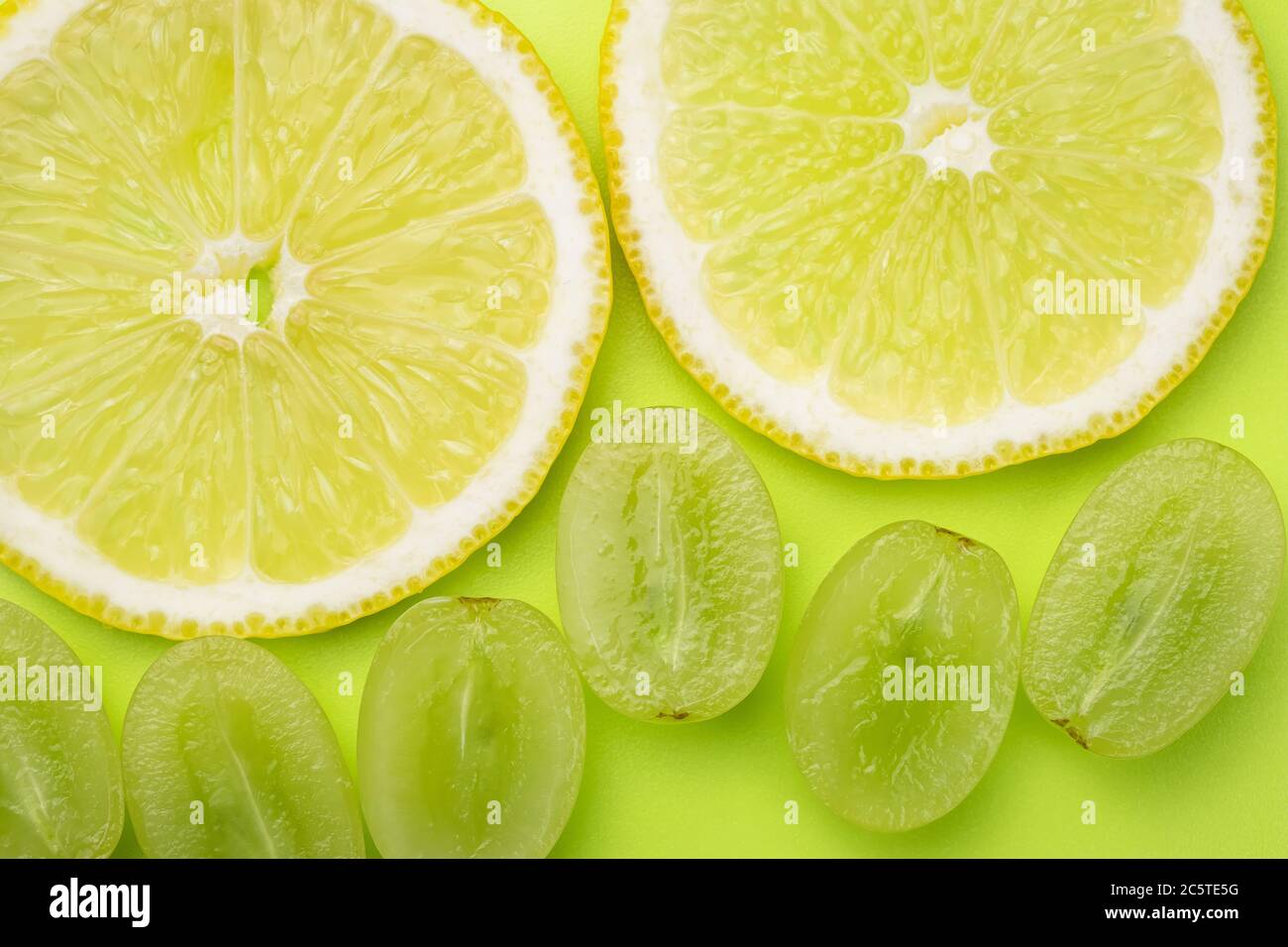 Una lonchas de limón y bayas de uvas blancas sobre un fondo de color verde  claro. Fondo de pantalla brillante de verano, patrón. Textura de color verde  y amarillo Fotografía de stock -