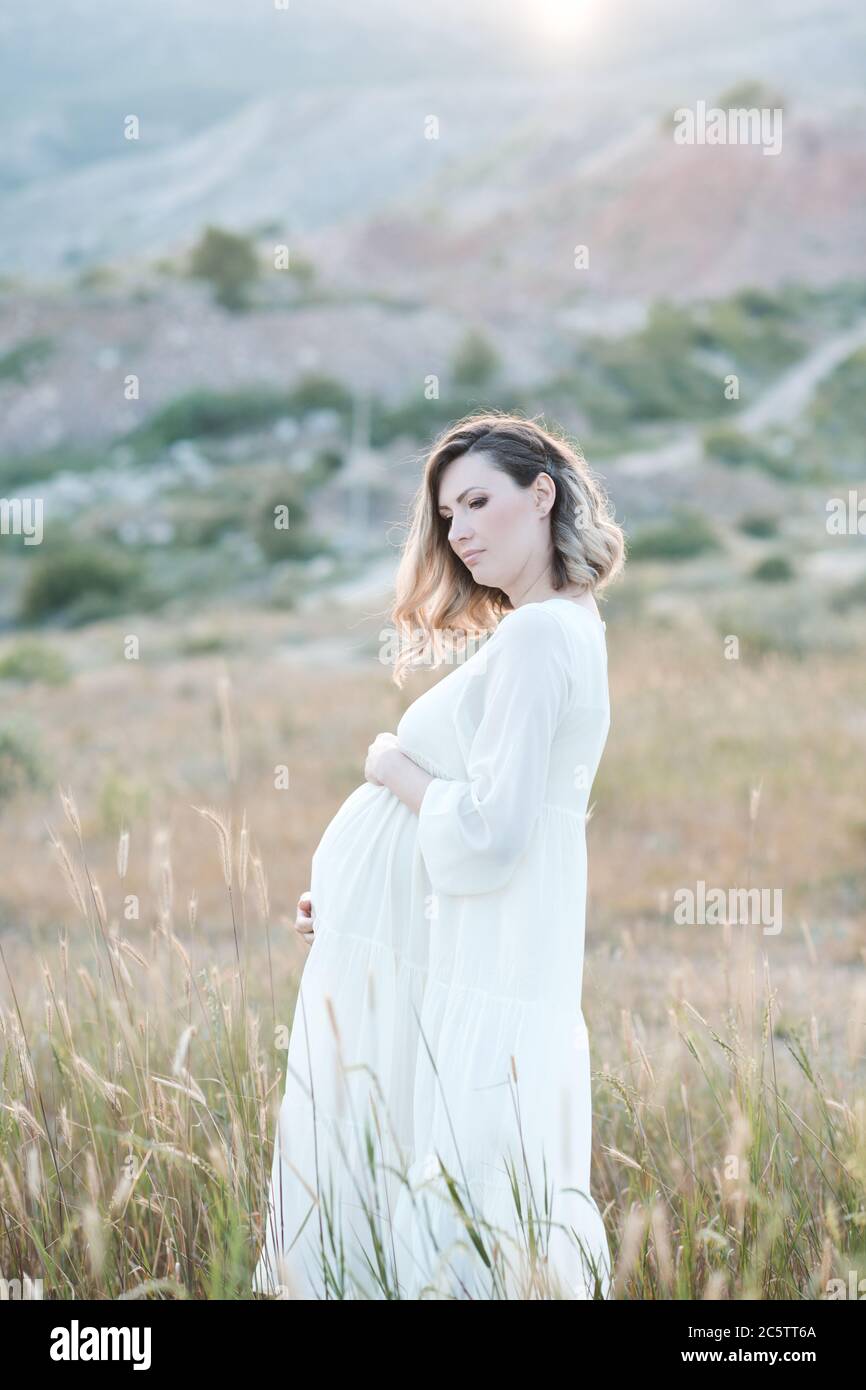 Mujer embarazada sonriente de 24-25 años de edad con elegante vestido  blanco posando en el campo al aire libre. Maternidad. Maternidad. 20 seg  Fotografía de stock - Alamy
