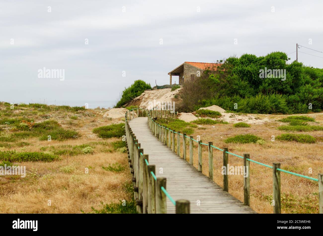 Puente que cruza las dunas más allá del horizonte, con una casa en la playa Foto de stock