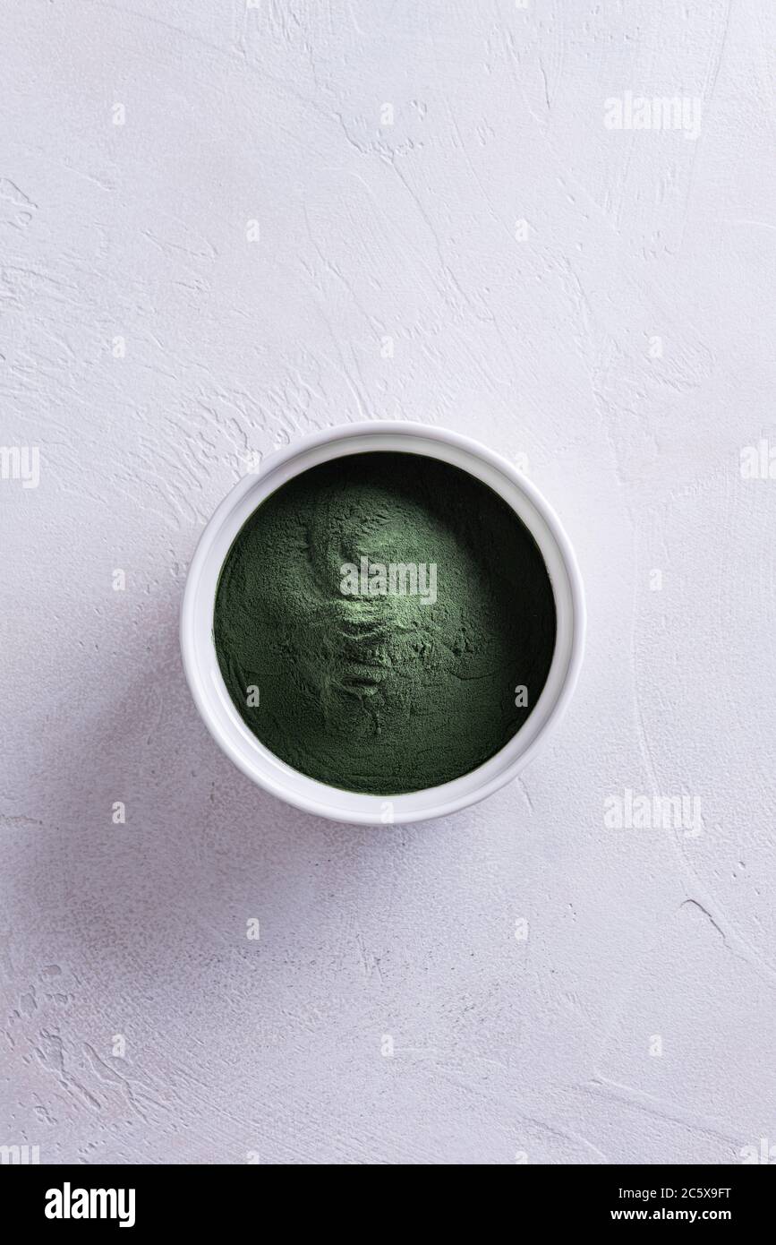 Polvo verde natural de clorela o espirulina en un tazón blanco redondo de porcelana directamente arriba. Concepto de alimentación y dieta saludable. El Tex. Blanco Foto de stock