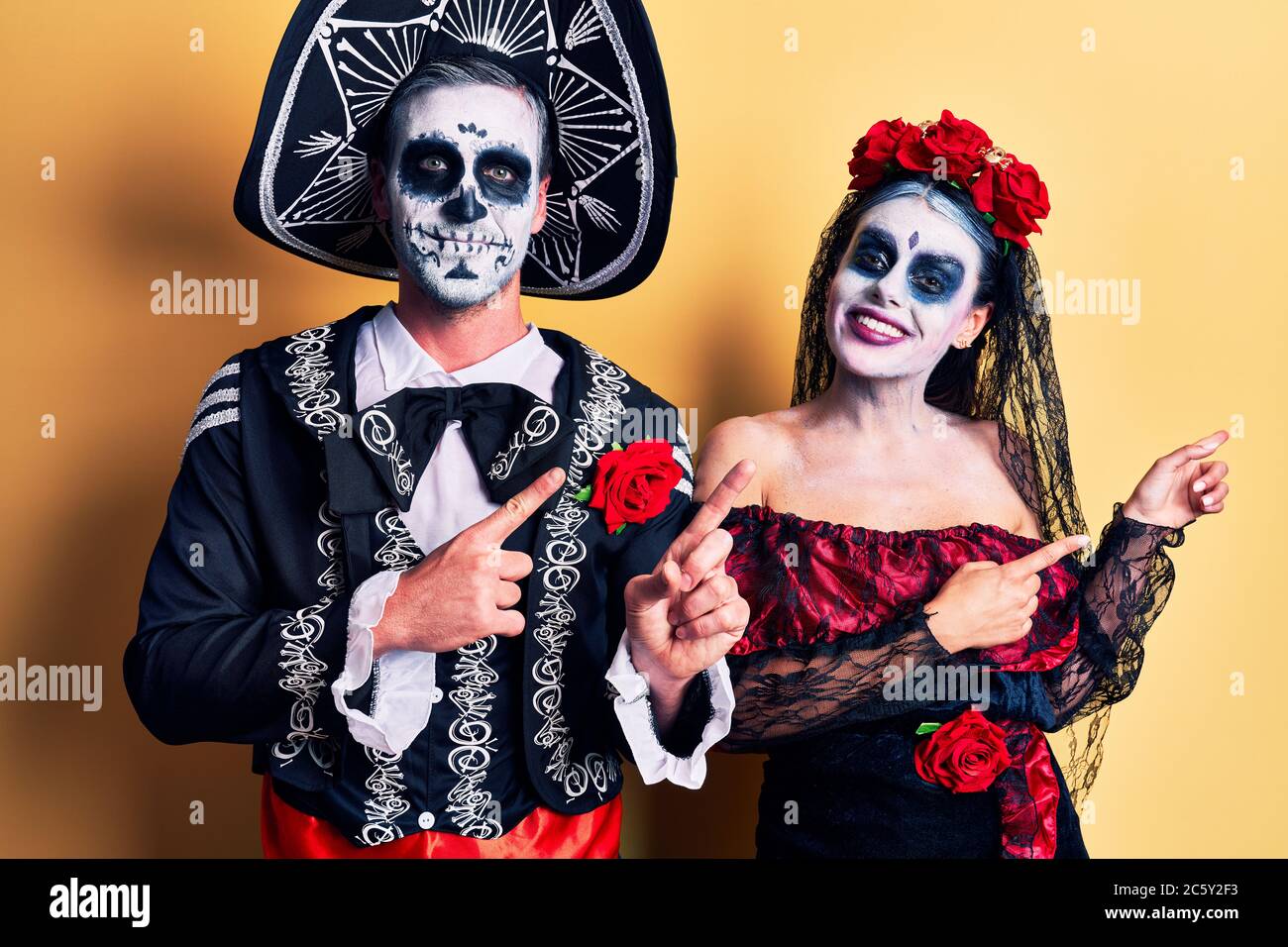 Pareja joven con el día mexicano de la muerte disfraz sobre amarillo  sonriendo y mirando la cámara apuntando con dos manos y dedos a un lado  Fotografía de stock - Alamy