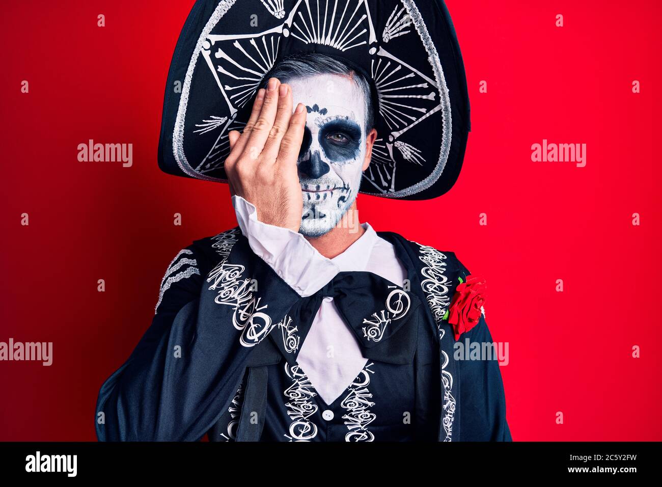 Joven que viste el día mexicano de la muerte disfraz sobre rojo que cubre  un ojo con la mano, sonrisa segura en la cara y emoción sorpresa Fotografía  de stock - Alamy