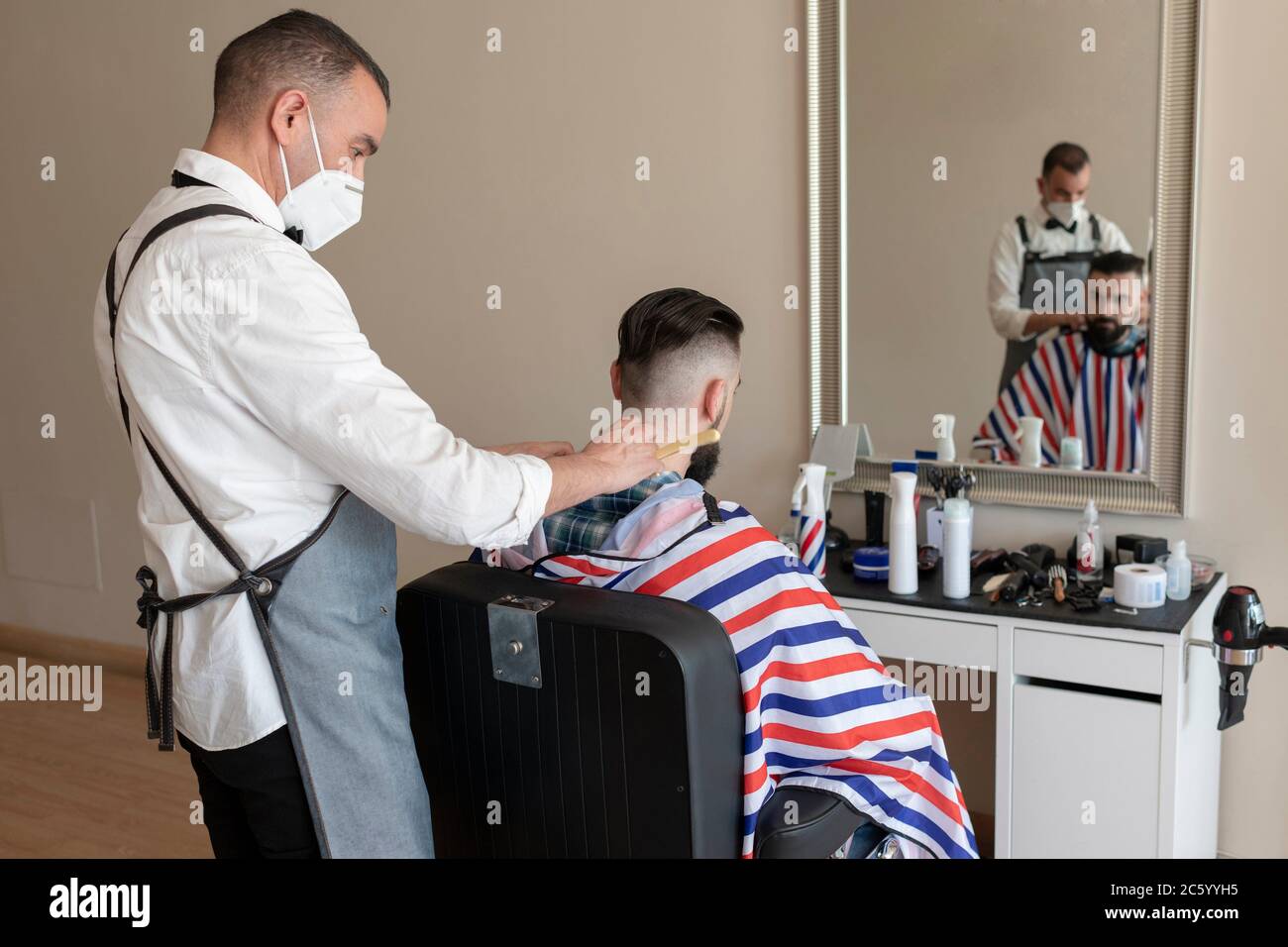 peluquería barbería en la peluquería a un cliente, ambos usan máscaras