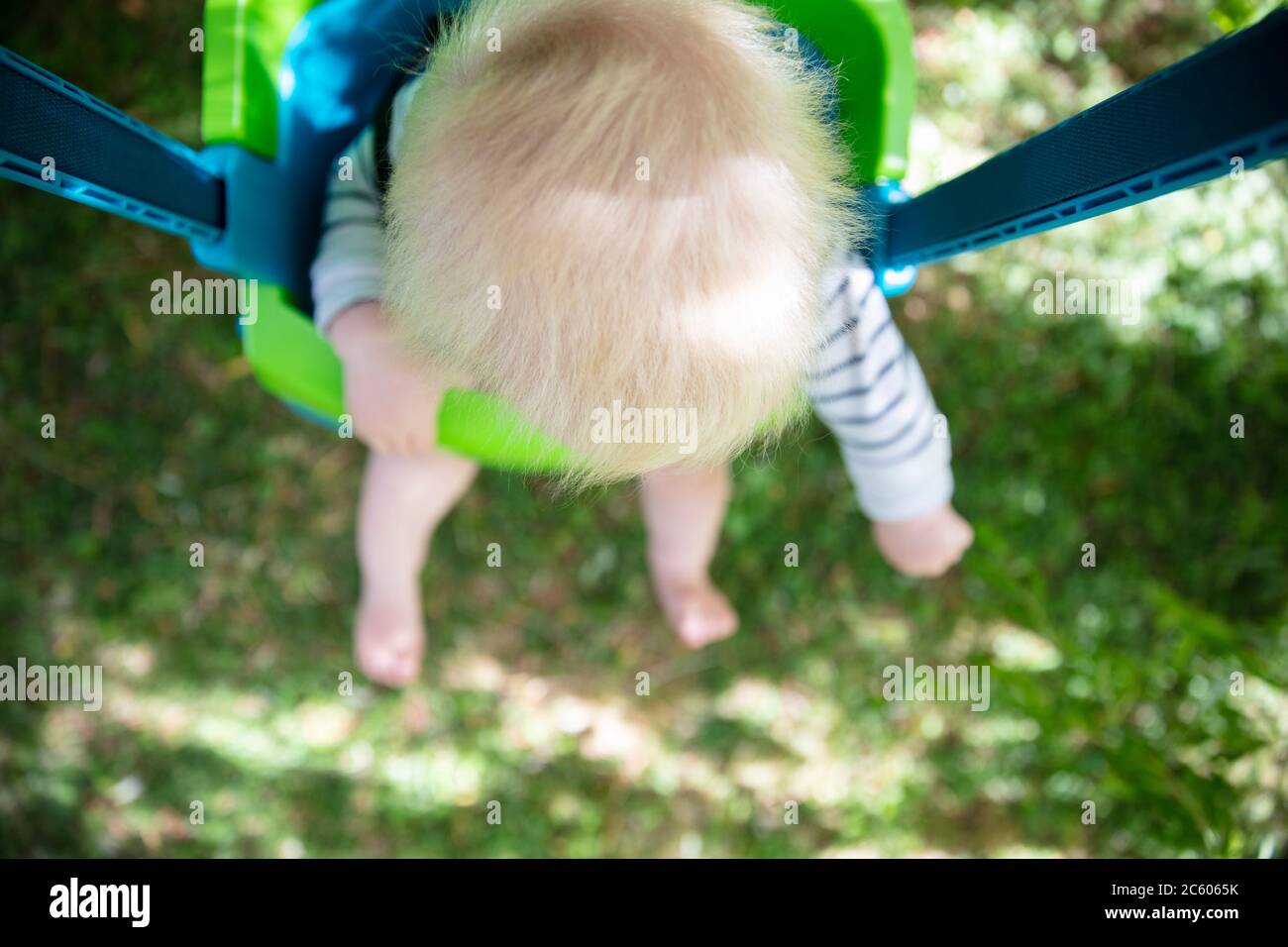 Un niño pequeño que se divierte jugando en un columpio bajo un árbol en un jardín Foto de stock