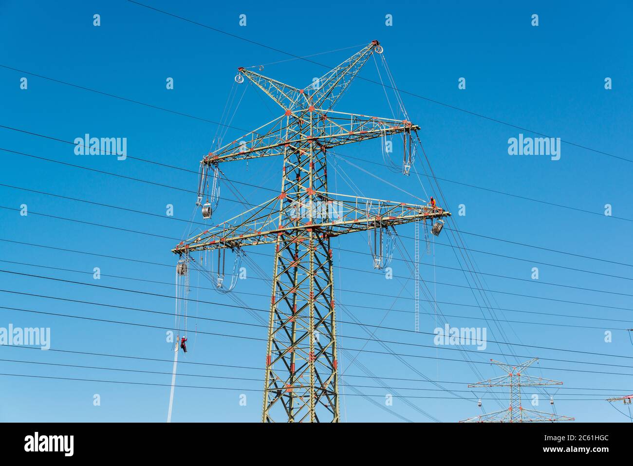 Arbeiter auf einem Hochspannungsmast vor blauem wolkenlosen Himmel Foto de stock
