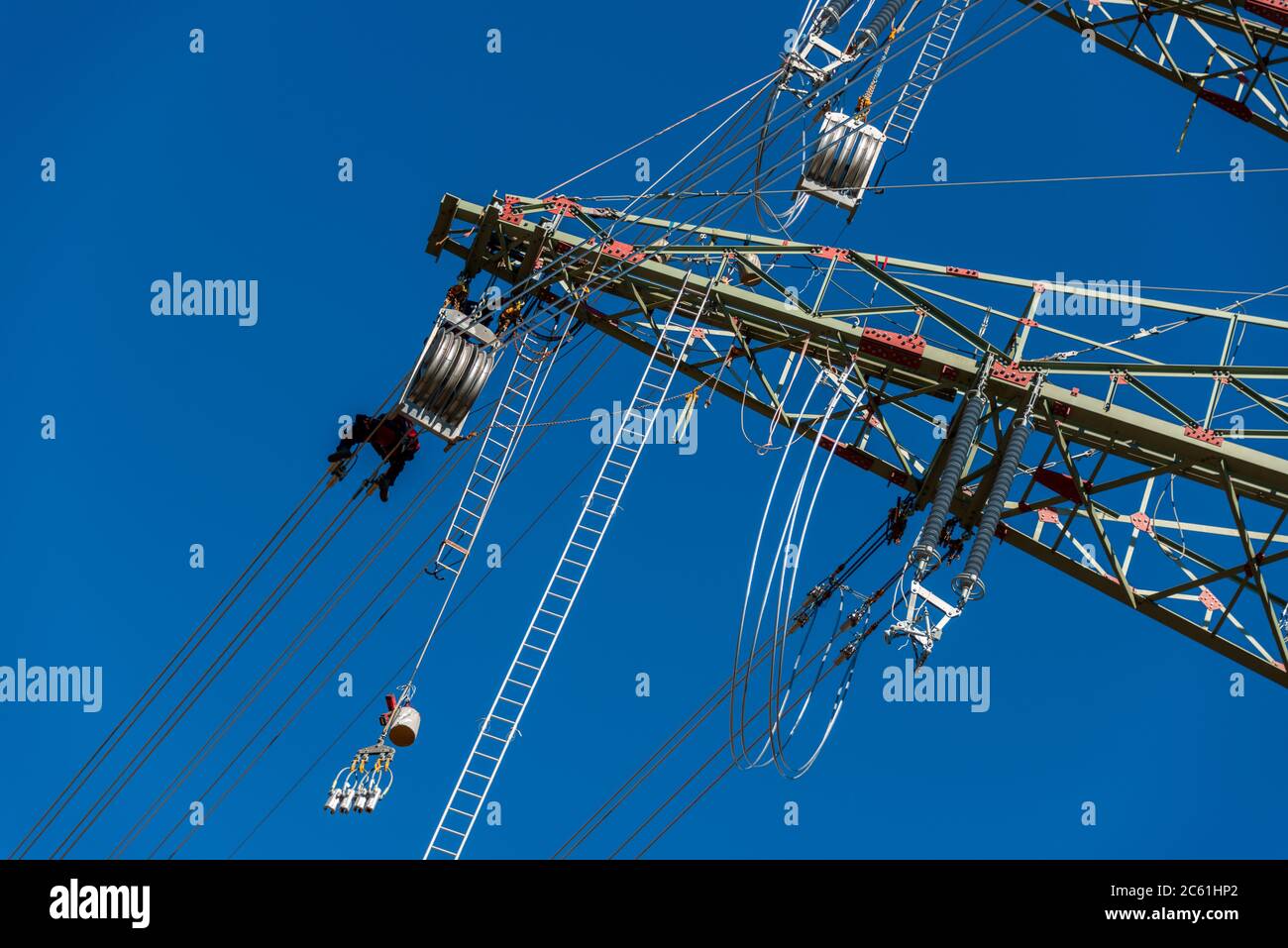 Arbeiter auf einem Hochspannungsmast vor blauem wolkenlosen Himmel Foto de stock