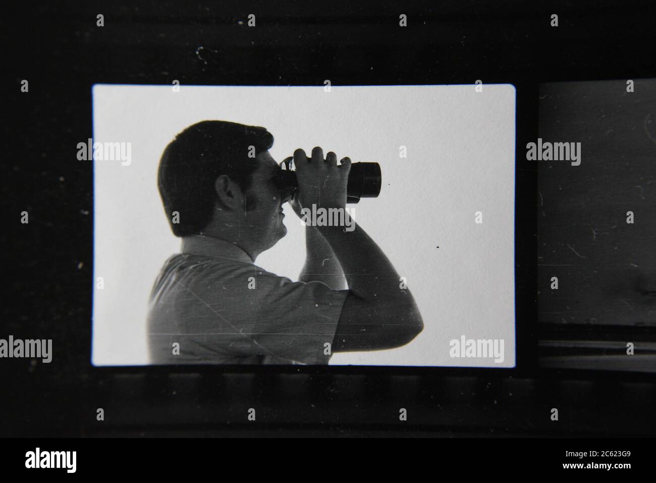 Foto en blanco y negro de un hombre mirando a través de sus binoculares mientras está en el trabajo. Foto de stock