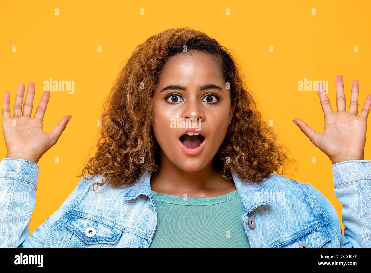Sorprendida joven afroamericana jadeando con las manos aisladas sobre fondo amarillo Foto de stock