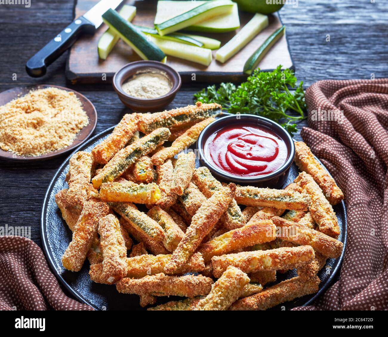 Crujientes palitos de calabacín empanadados con pan rallado, queso parmesano, especias en un plato con ketchup, merienda saludable de verano con comida para los dedos, vista desde un Foto de stock