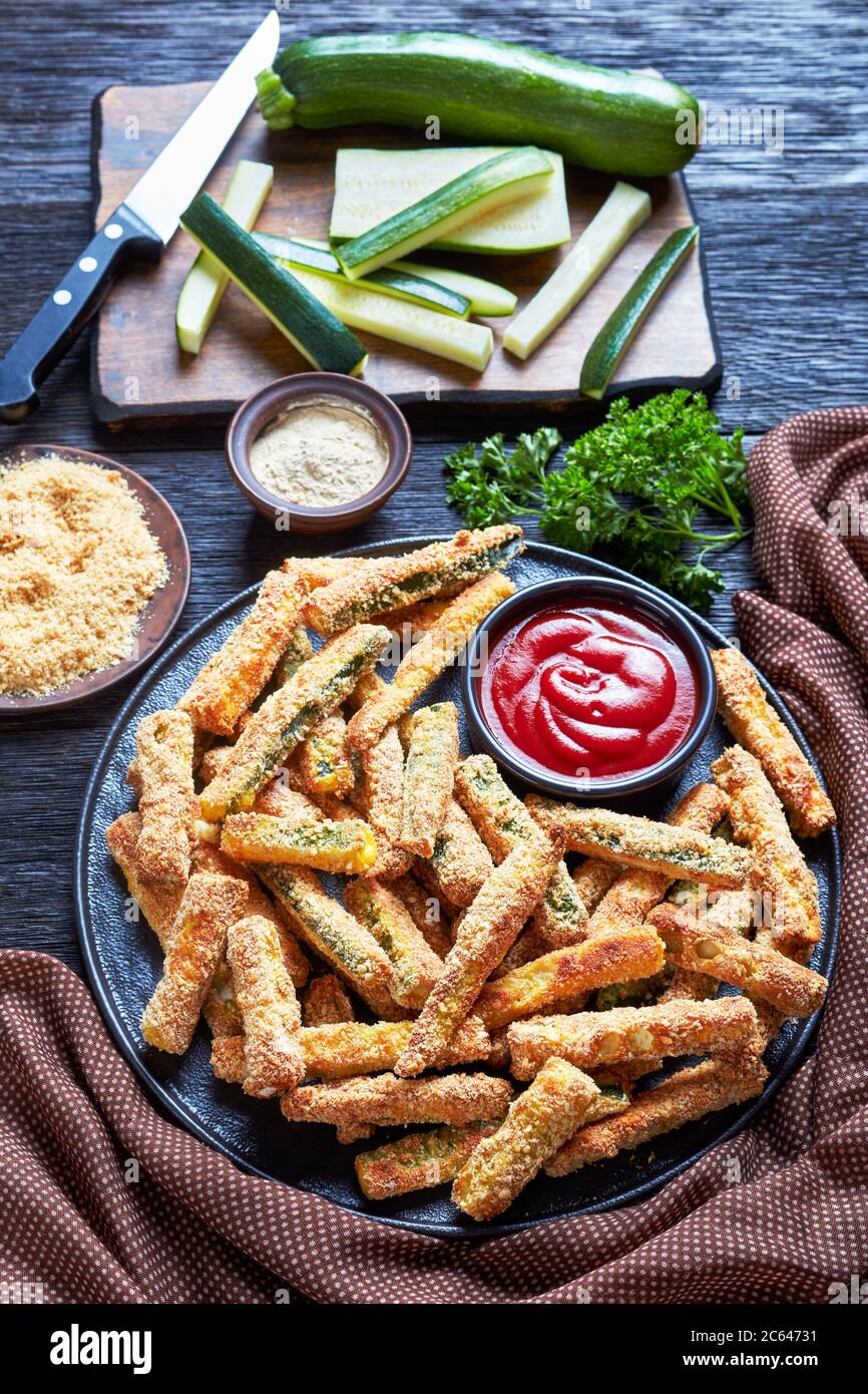 Crujientes palitos de calabacín empanados con pan rallado, queso parmesano, especias en un plato con ketchup, merienda saludable de verano con comida para los dedos, vi vertical Foto de stock