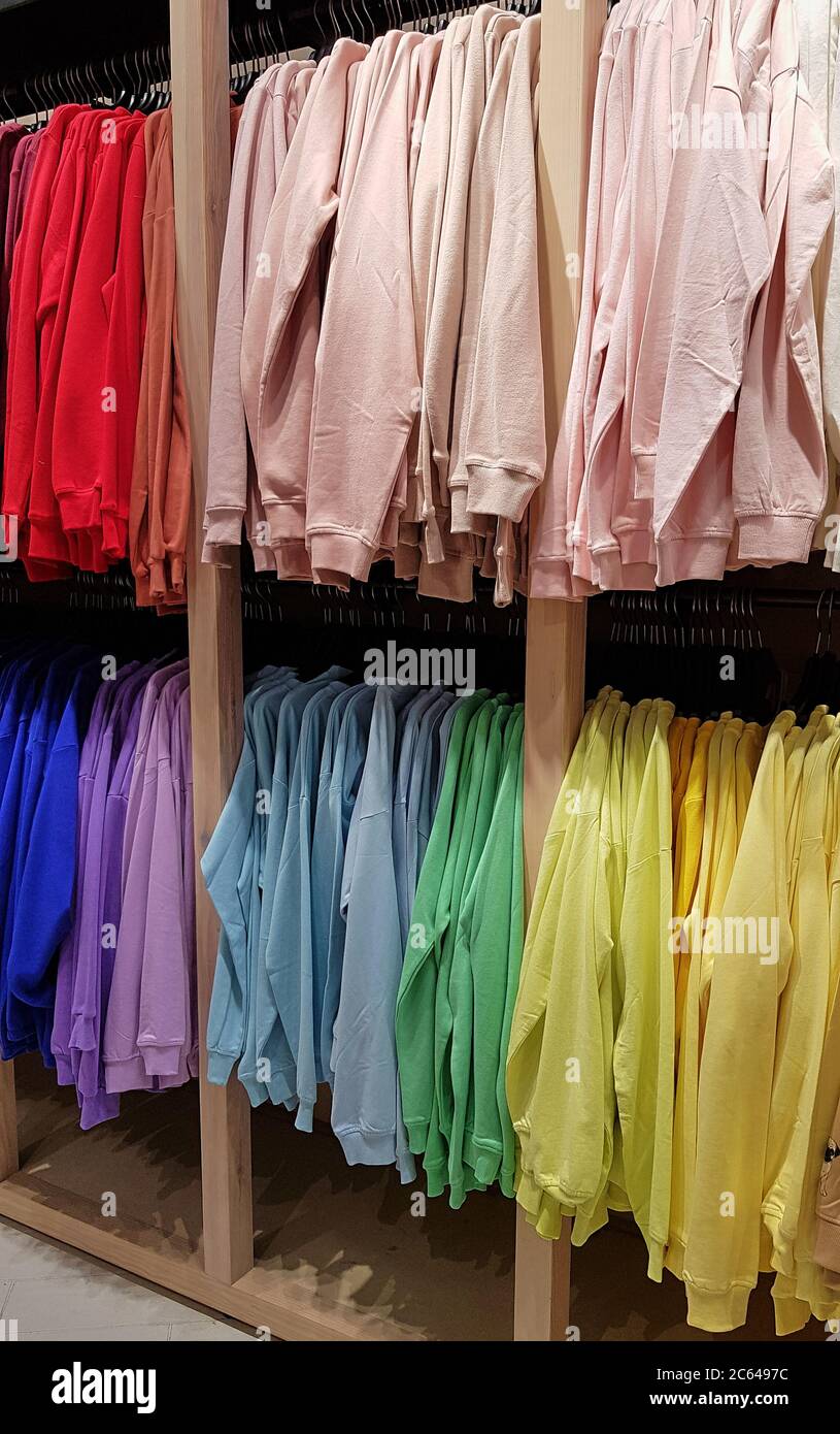 Sudaderas y brillantes colgadas en una tienda de moda. Primer plano de sudaderas multicolor amarillas, rojas, rosadas y géen cuelgan en fila en un suspensor Fotografía de stock - Alamy