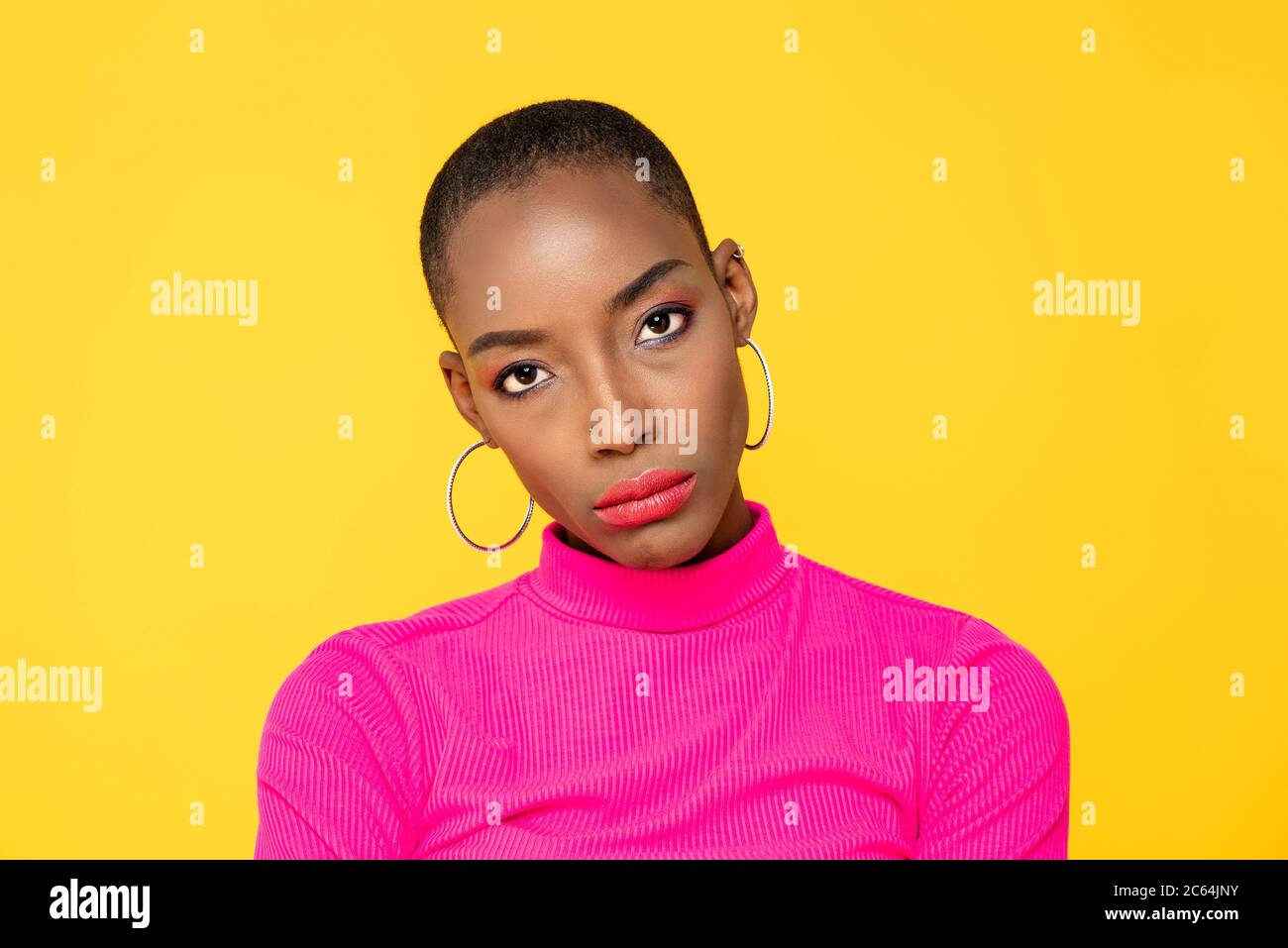 Primer plano retrato de una joven afroamericana infeliz frunciendo el ceño con la cámara en un estudio aislado de fondo amarillo Foto de stock