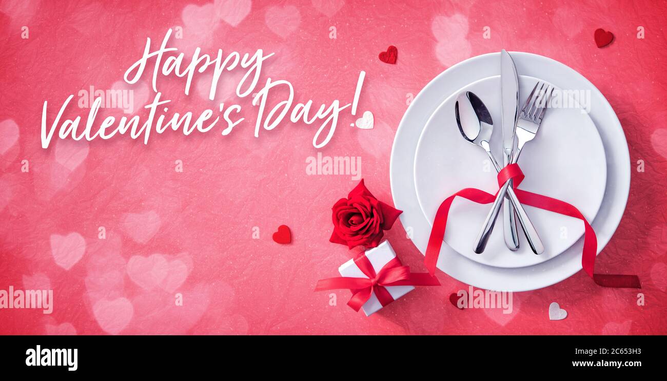 Mesa roja cubiertos con decoración de corazones, caja de regalo y rosa para la cena de los días de San Valentín Foto de stock